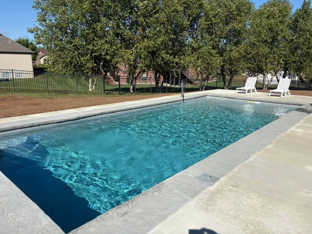 Modern rectangular fiberglass pool with tanning ledge, clear blue water, and spacious concrete decking in a Columbia, IL backyard.