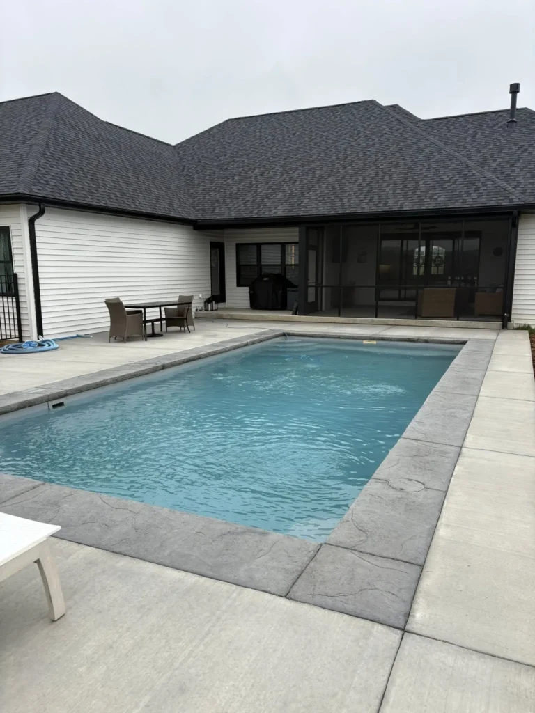 Custom rectangular fiberglass swimming pool with screened-in porch, concrete patio, and low-maintenance backyard design in Columbia, Illinois.