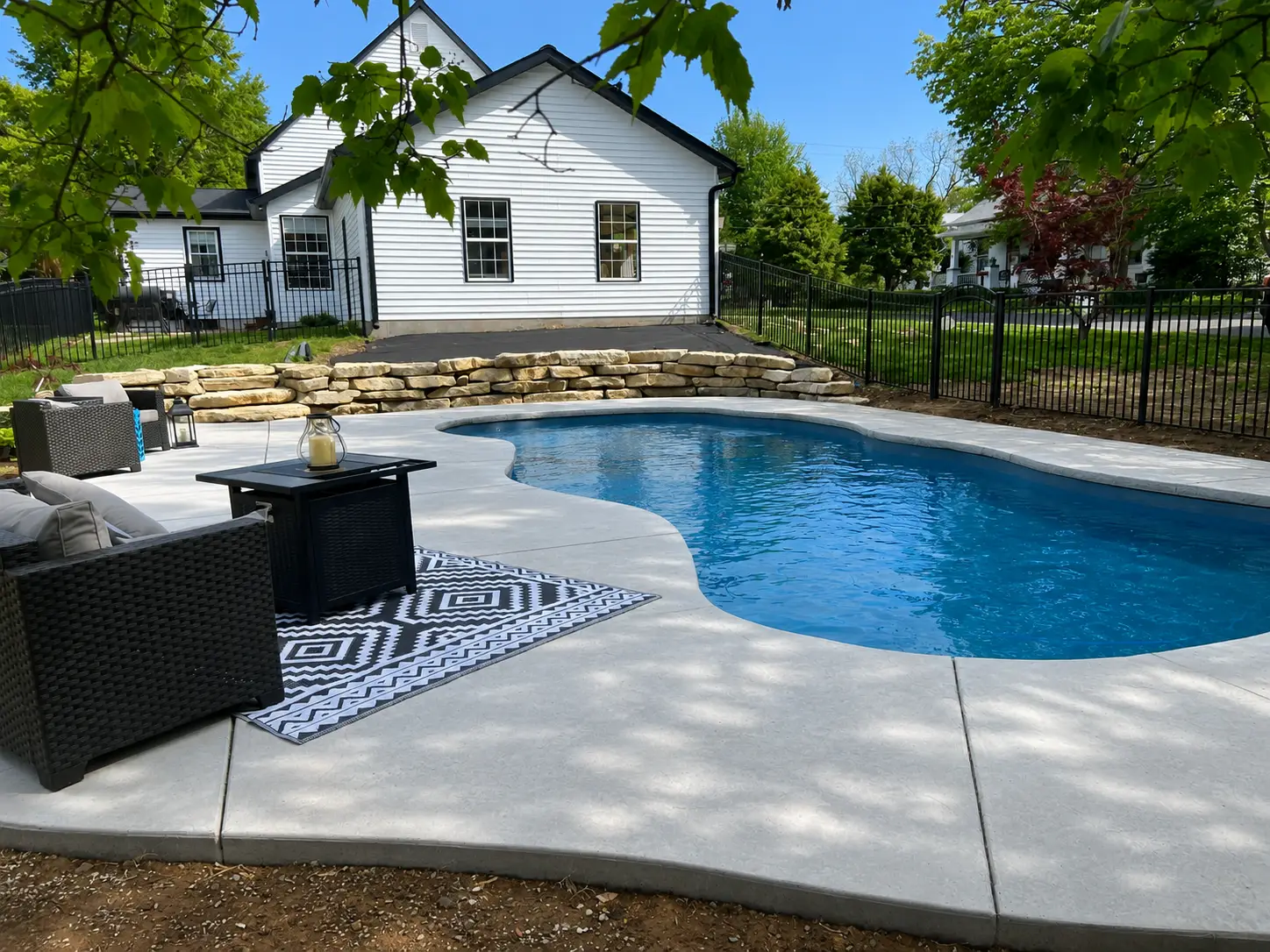 Custom fiberglass swimming pool with modern outdoor seating, stone retaining wall, and fenced backyard in Columbia, Illinois.