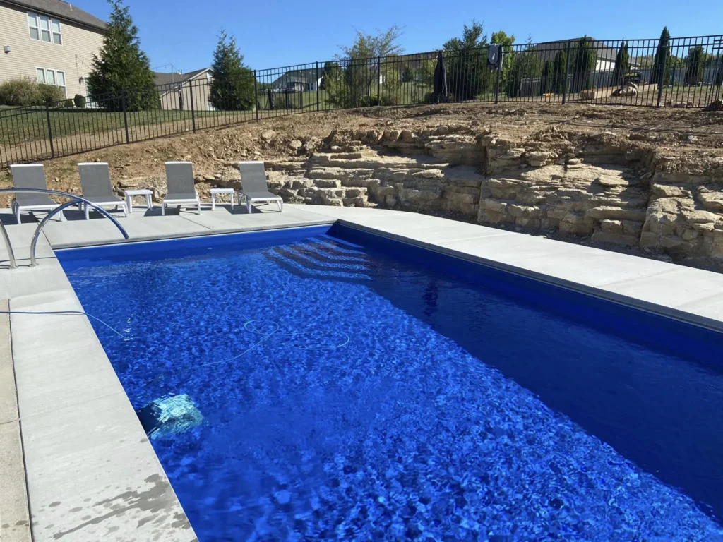 Luxury rectangular fiberglass pool with built-in entry steps, rock retaining wall, and poolside lounge seating in Columbia, IL.