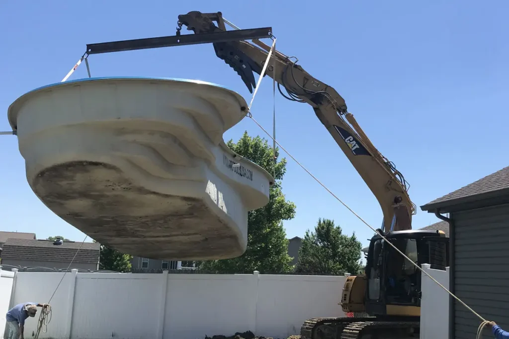 Fiberglass pool shell installation using heavy equipment and crane attachment at a residential property in Columbia, Illinois.