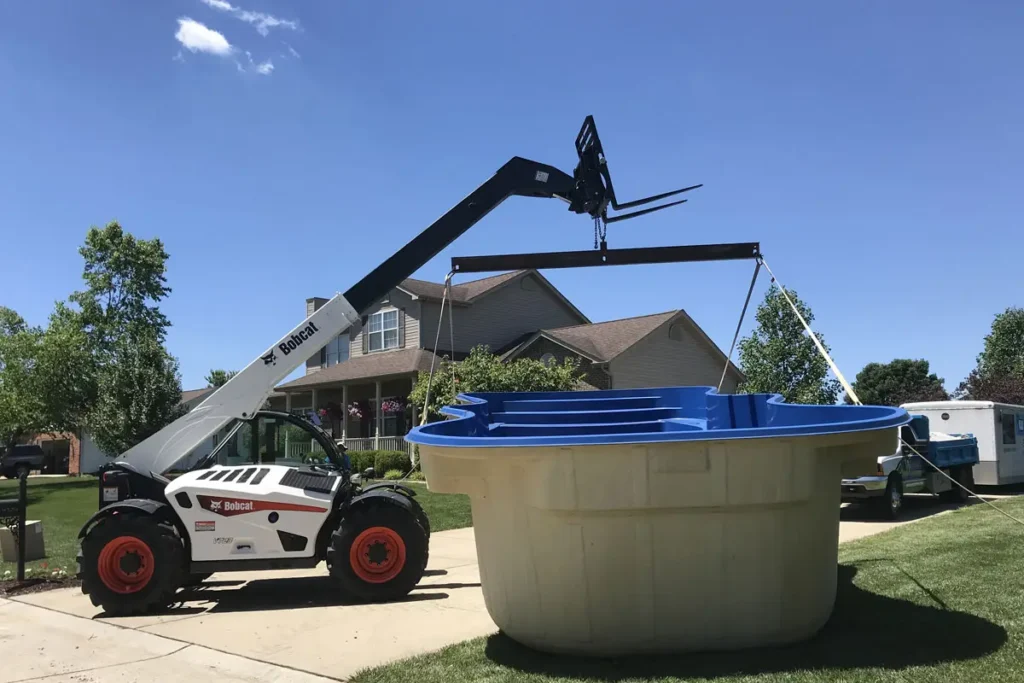 Fiberglass pool shell delivery and placement using Bobcat telehandler during pool construction in Columbia, IL.