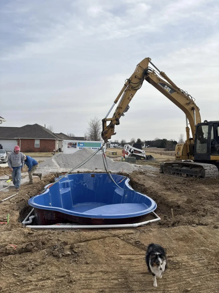 Fiberglass pool installation in progress with excavator placing pool shell into prepared excavation site in Columbia, Illinois.