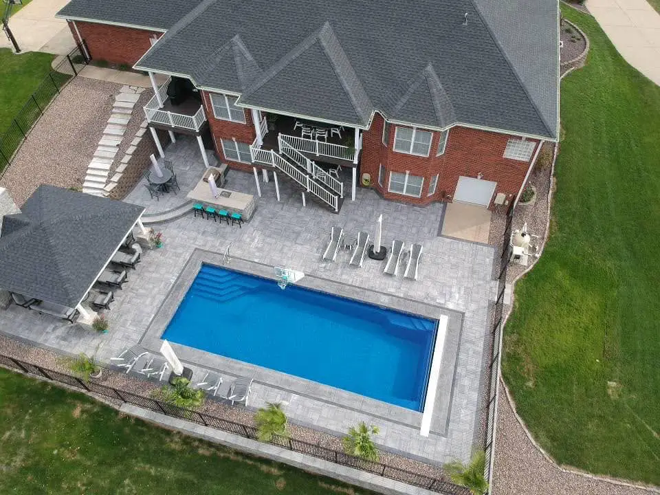 Aerial view of luxury rectangular fiberglass pool with paver patio, pavilion, outdoor kitchen, and custom backyard design in Columbia, Illinois.