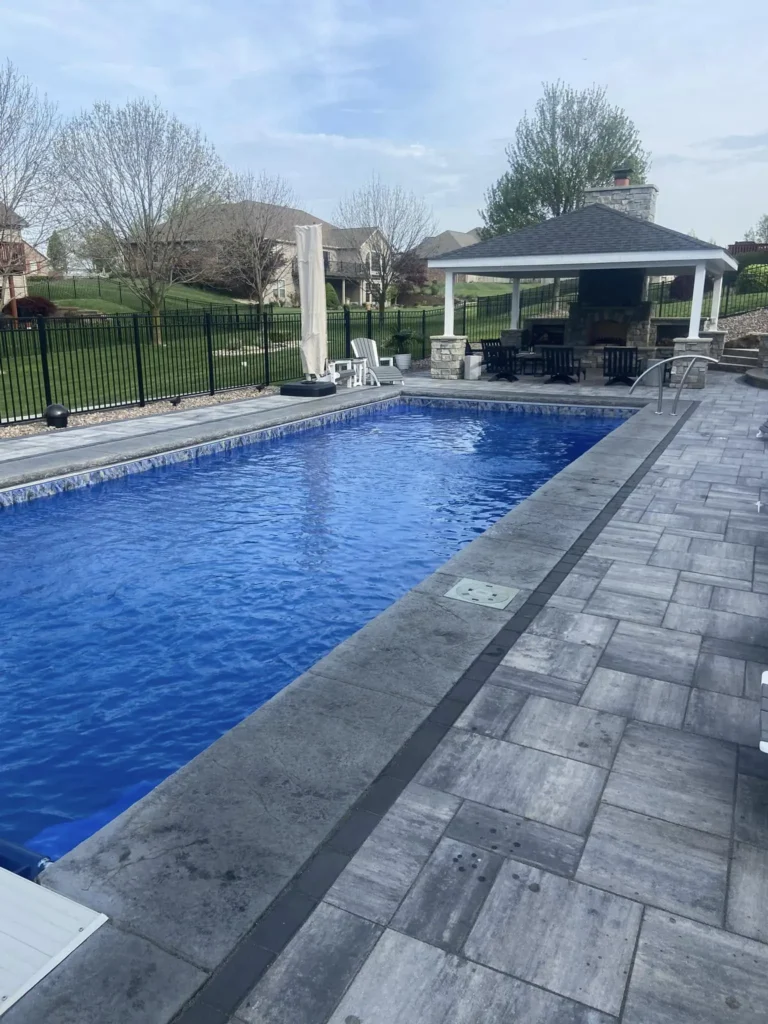 Luxury rectangular fiberglass pool with pavilion, outdoor fireplace, and custom paver patio in a Columbia, IL backyard.