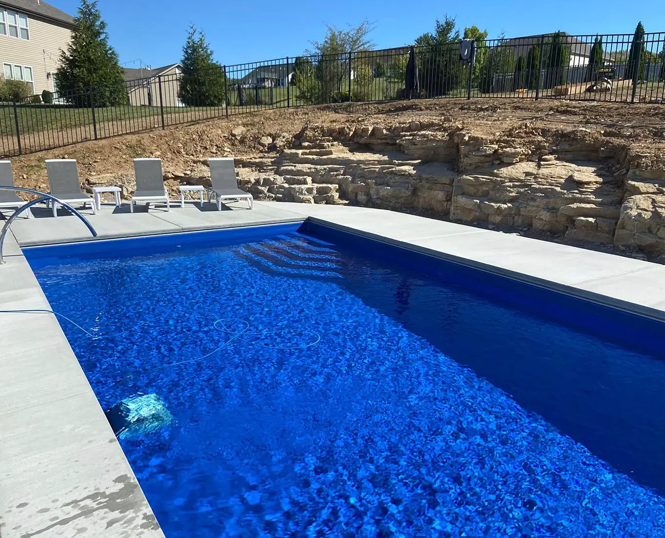 Residential fiberglass pool featuring clear water, retaining wall construction, and a beautifully designed backyard setting in Smithton, IL.