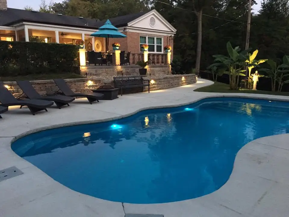 Fiberglass pool with stamped concrete patio and black lounge chairs in a spacious Columbia, IL backyard.